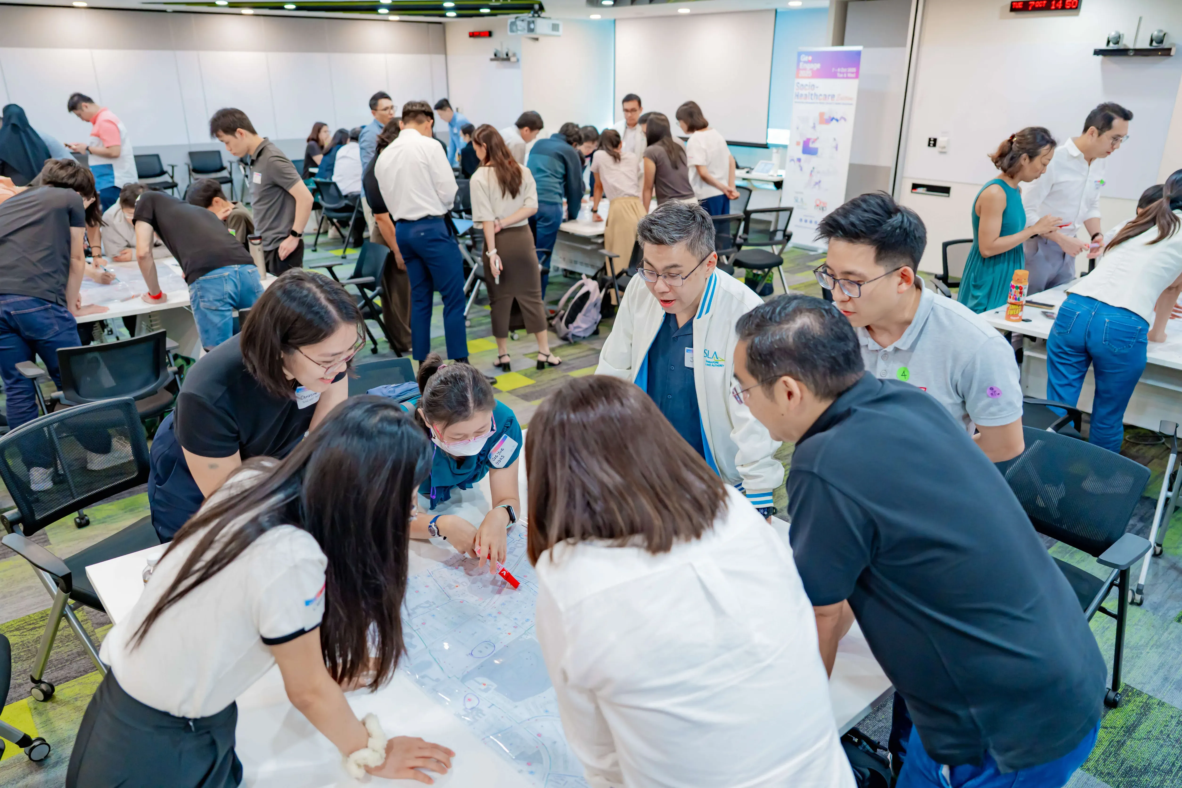 A group of people gathered around tables in a conference room, collaborating over printed maps and documents.